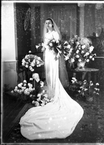 Montbéliard, (Doubs). Mariage Willermoz, la mariée avec sa traîne, pose seule dans un salon ornementé de gerbes de fleurs : plaque de verre 13x18 cm.