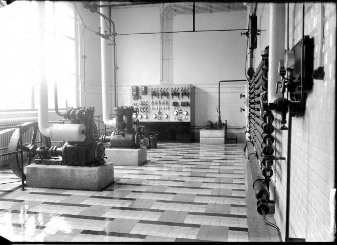 Une salle carrelée avec des machines industrielles à courroie de la marque Sté Usines Quiri : plaque de verre 13x18 cm.