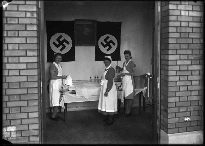 Dans un petit local en briques jaunes de la SNCF. Trois infirmières préparent des biberons de lait sous le portrait d'Hitler entouré de deux drapeaux à croix gammée.