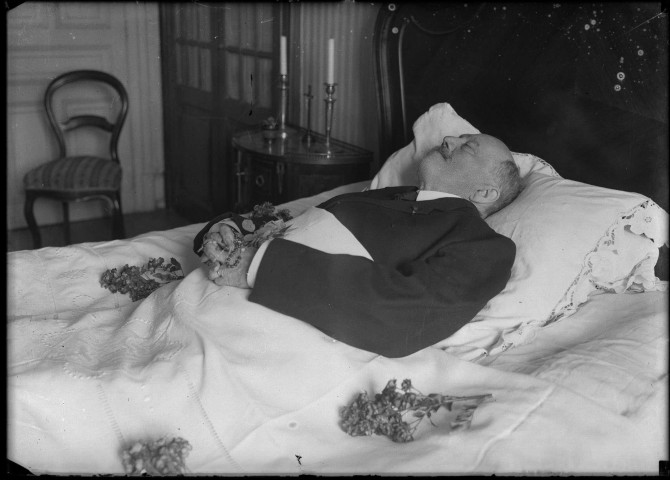 Une chambre, le corps d'un homme reposant sur son lit de mort, dans ses mains jointes il tient un chapelet, autour de lui quelques fleurs sont disposées sur le drap : plaque de verre 13x18 cm, [s.l.].
