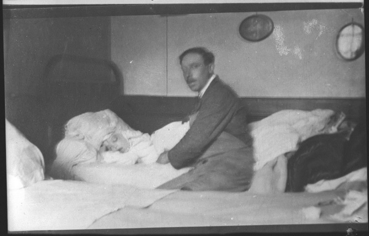 Dans un lit, les yeux fermés un bandage autour de la tête, un parent est assis sur le bord du lit : négatif souple 9x12 cm.