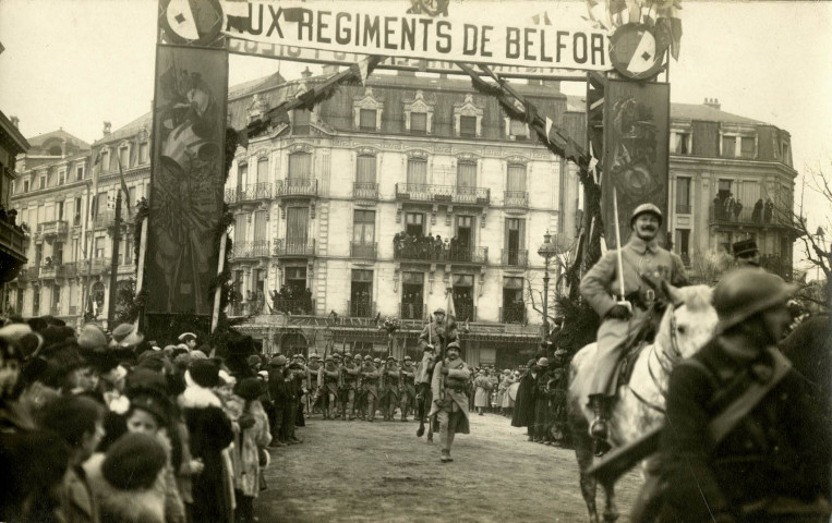 [Belfort, Place de la République], devant les grilles de la Préfecture, défilé militaire en l'honneur des régiments de Belfort. Passage du cortège sous un arc de triomphe