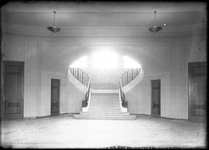 Vue intérieure, hall d'entrée avec son grand escalier réservé à l'administration, vue surexposée.