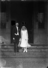 Devant [la mairie ou une demeure], un couple de mariés prend la pose sur les marches de la bâtisse.